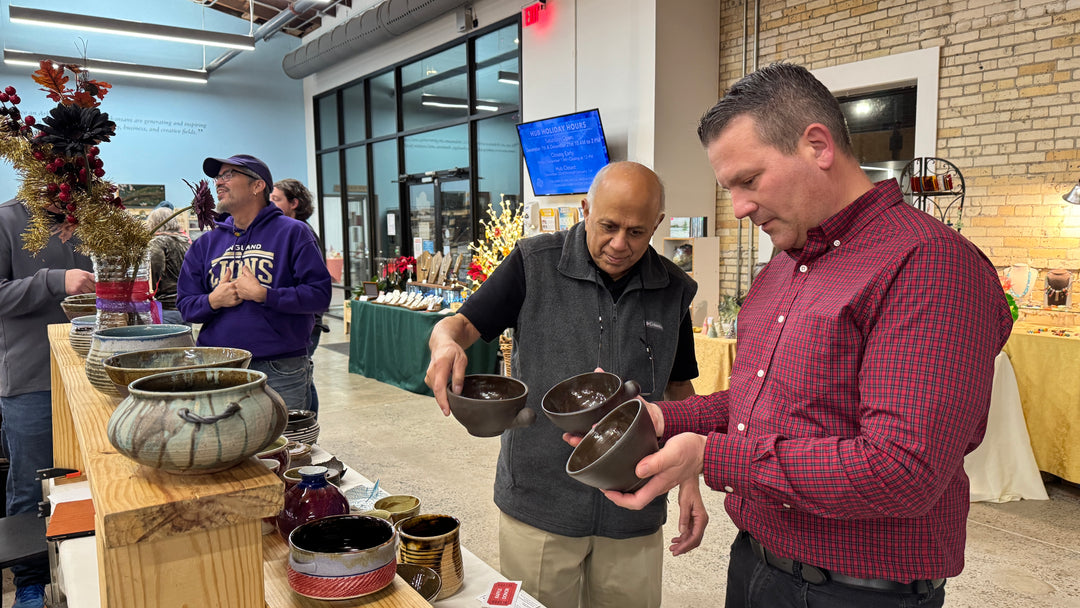 Two men examining finished clay soup bowls at the Make It Merry Market craft fair inside the Innovation Hub.