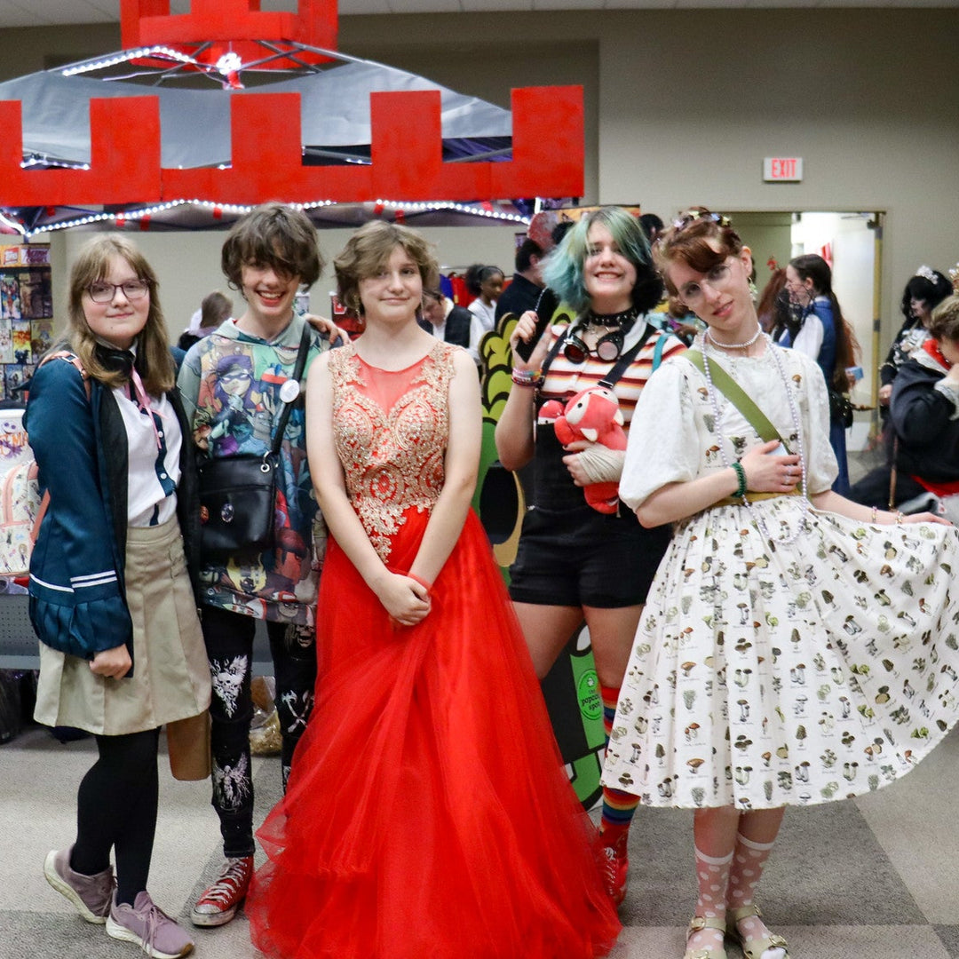 Group of people in cosplay posing together in the Vendor alley of Laman Con 2024 with a red and gray castle booth in the background.