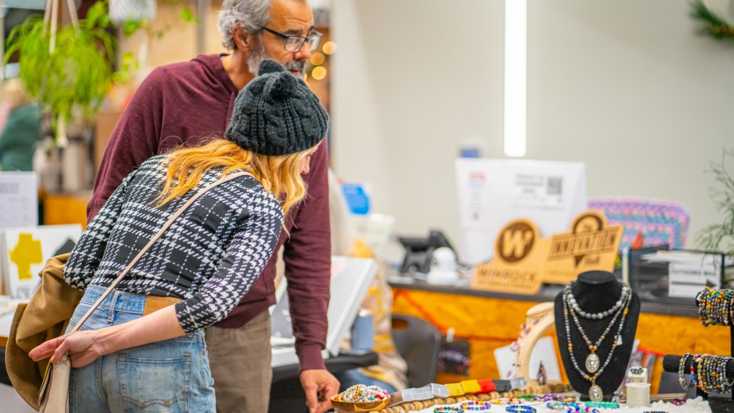 Two people shopping at the indoor  craft fair at the Hub with various items on display.