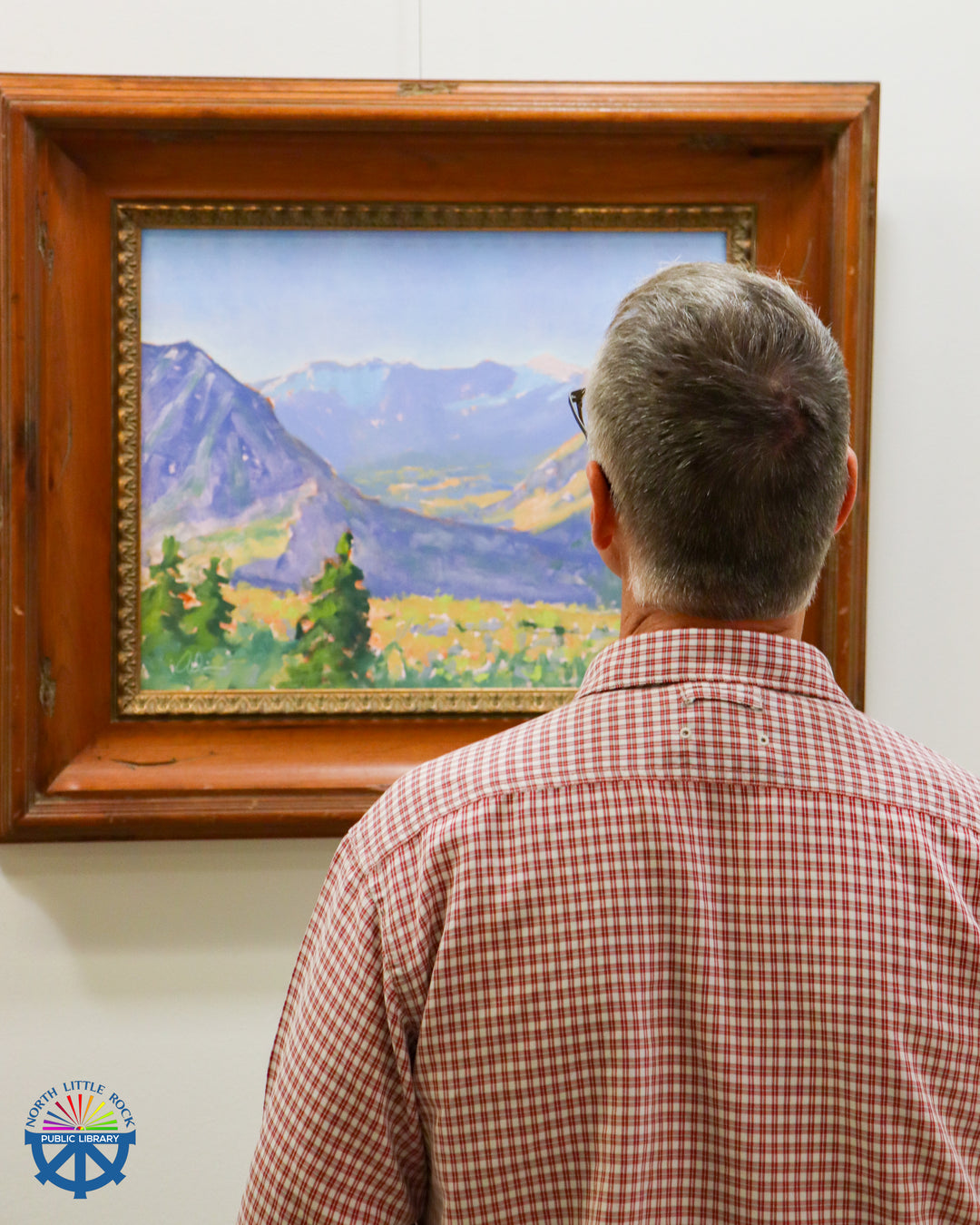 Man looking at a painting of a mountain landscape in a wooden frame.