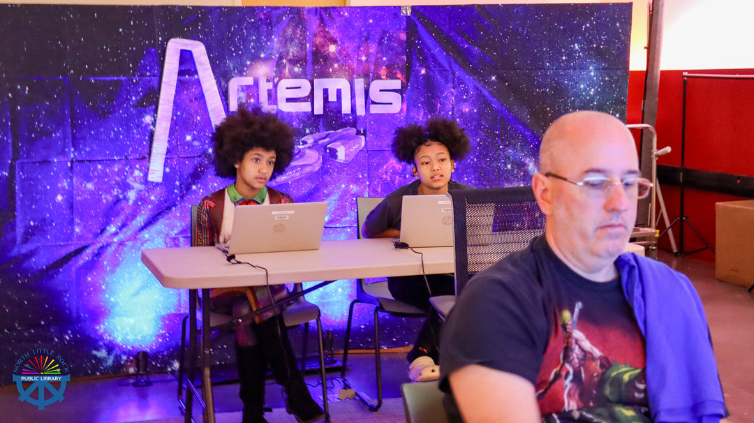 Two people sitting at a table with laptops in front of an 'Artemis' banner.