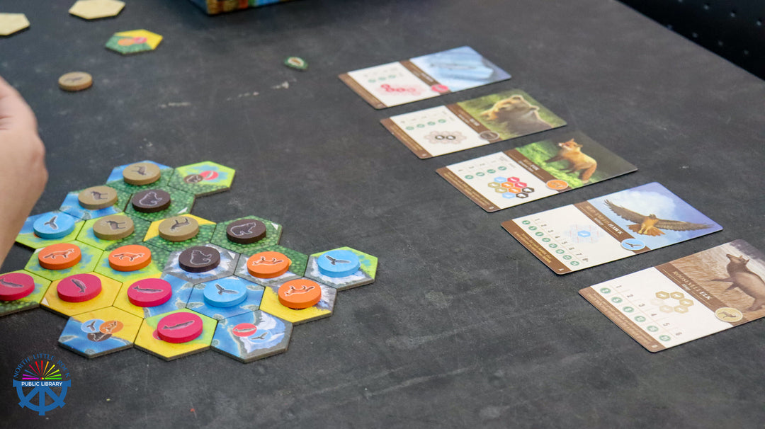 Board game with colorful hexagonal tiles and nature-themed cards on a dark surface