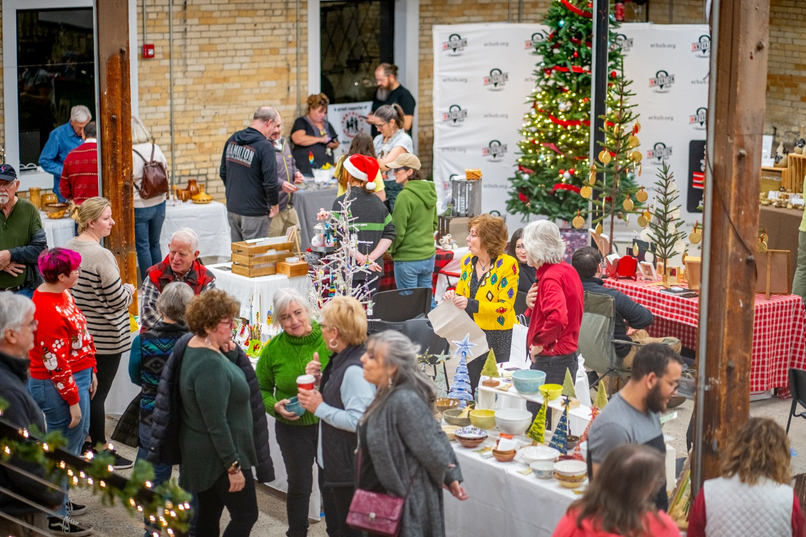 People gathered inside the Innovation Hub at a festive Make It Merry Market event with Christmas decorations, pottery, gifts, and food.
