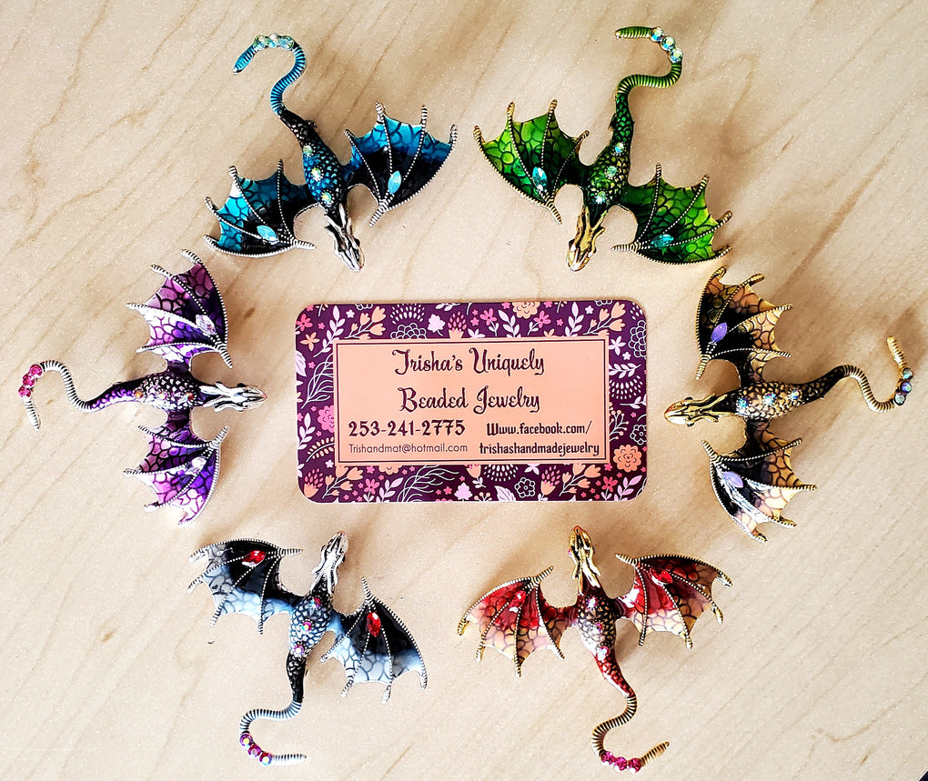 Colorful dragon-shaped jewelry pieces on a wooden surface with a business card for 'Jewelry'.