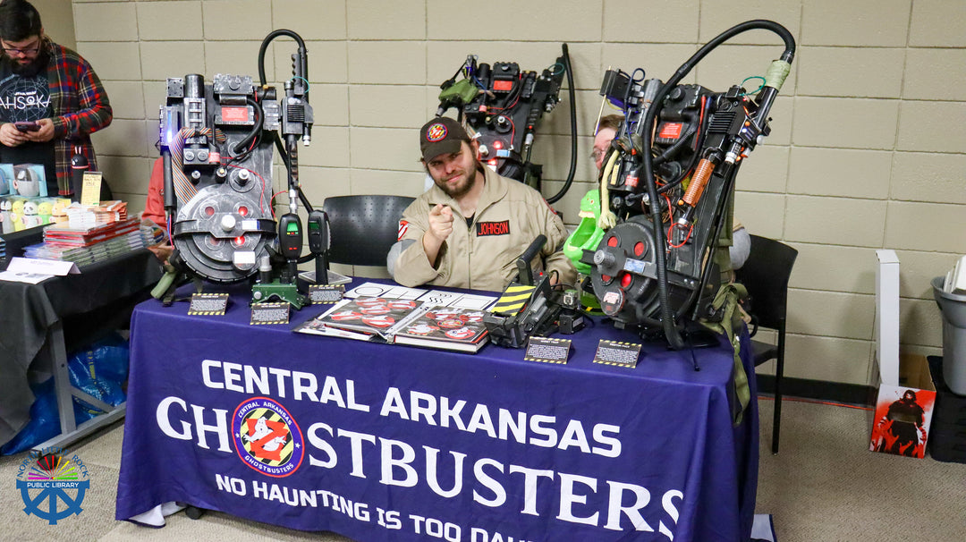 Person sitting at a table with Ghostbusters-themed props and signage in a room.